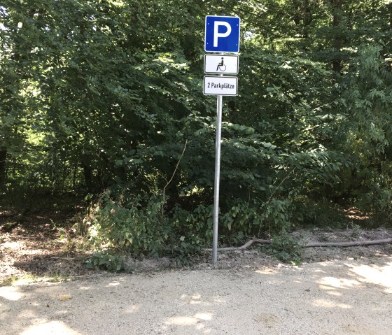 Ein Parkplatzschild für Behinderte im Wald. Es zeigt zwei verfügbare Parkplätze an. Umgeben von dichtem Grün und Bäumen., © TI Bitburger Land Ein Parkplatzschild für Behinderte im Wald. Es zeigt zwei verfügbare Parkplätze an. Umgeben von dichtem Grün und Bäumen., © TI Bitburger Land