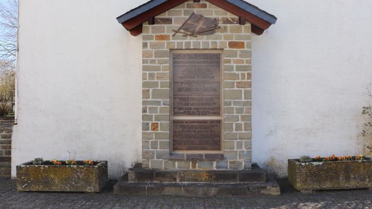 A stone-built building with a wooden overhang. In front of the building, there are two planters.