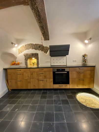 A modern kitchen with wooden cabinets and a black stove. In the background, a rustic stone oven is visible.