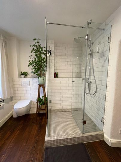 A modern bathroom with a glass shower and white tiles. A plant and a wooden bench create a pleasant atmosphere.