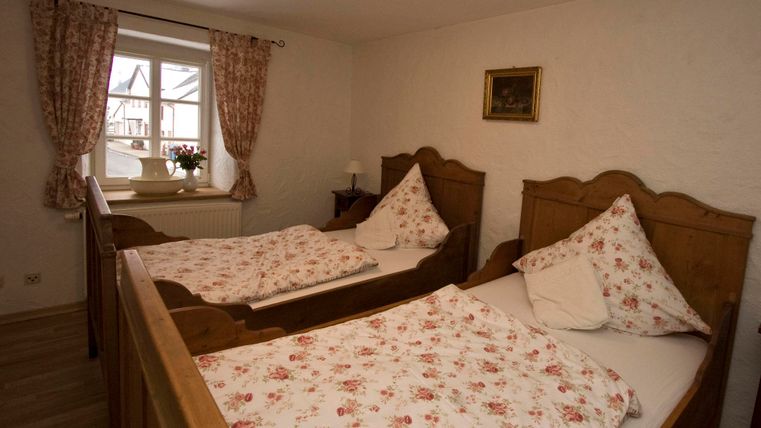 Ein gemütliches Schlafzimmer mit zwei Einzelbetten aus Holz und blumiger Bettwäsche. Das Fenster lässt viel Licht herein und gibt einen Blick nach draußen.