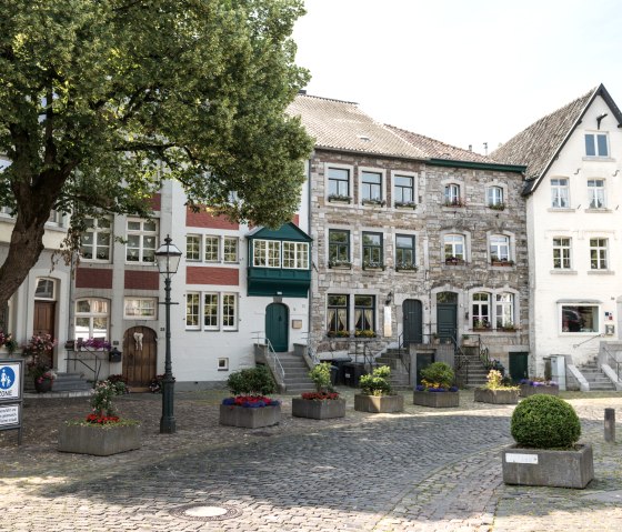 Historische Häuser in Kornelimünster mit Kopfsteinpflaster, Blumenbeeten und einem großen Baum im Vordergrund., © Eifel Tourismus GmbH, D. Ketz