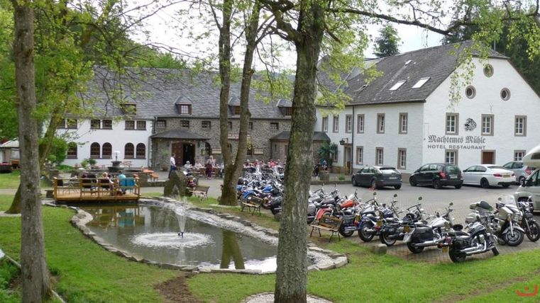 Ein malerisches Restaurant mit einem kleinen Teich und Bäumen. Vor dem Gebäude stehen viele Motorräder geparkt.