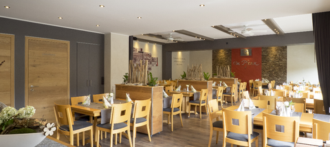 Ein modernes Restaurant mit Holztischen und -stühlen. Die gemütliche Atmosphäre wird durch sanfte Beleuchtung und dekorative Elemente unterstrichen.