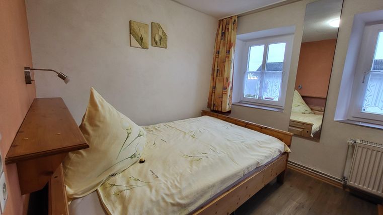 Ein gemütliches Schlafzimmer mit einem Einzelbett und warmen Farben. Große Fenster bringen viel Licht in den Raum.