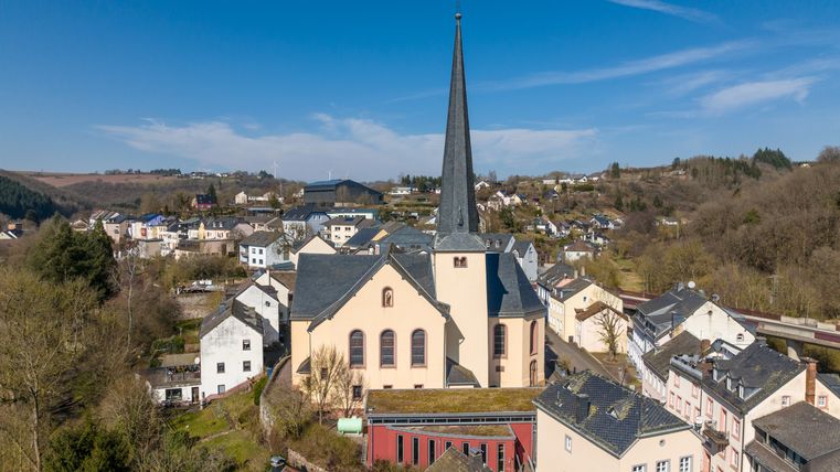 Luftaufnahme von Waxweiler mit der Kirche im Zentrum und umliegenden Häusern.