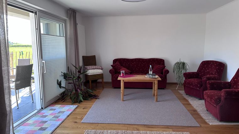 A cozy living space with red sofas and a wooden table. Large windows let in plenty of light and offer a view outside.