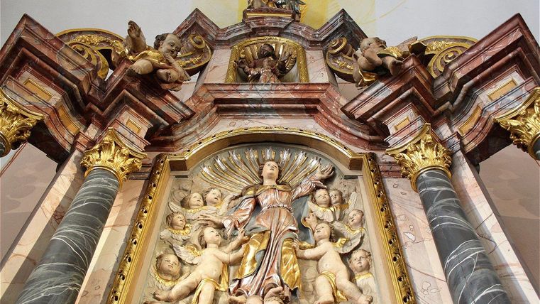 Ein kunstvoller Altar mit goldenen und marmorierten Details. Die zentrale Figur zeigt eine Heilige umgeben von Engeln und Putten.
