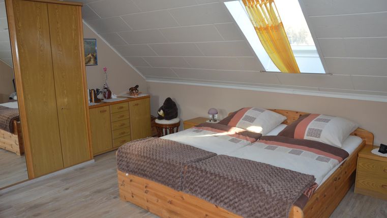 Ein gemütliches Schlafzimmer mit einem Doppelbett und hellen Wänden. Großes Fenster und Holzschränke sorgen für eine einladende Atmosphäre.
