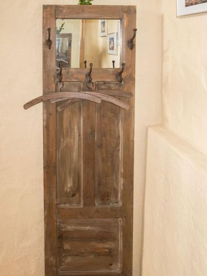 Ein rustikaler Holzschrank mit einem Spiegel und mehreren Kleiderhaken. Die Wände sind in einem sanften Beigeton gehalten.