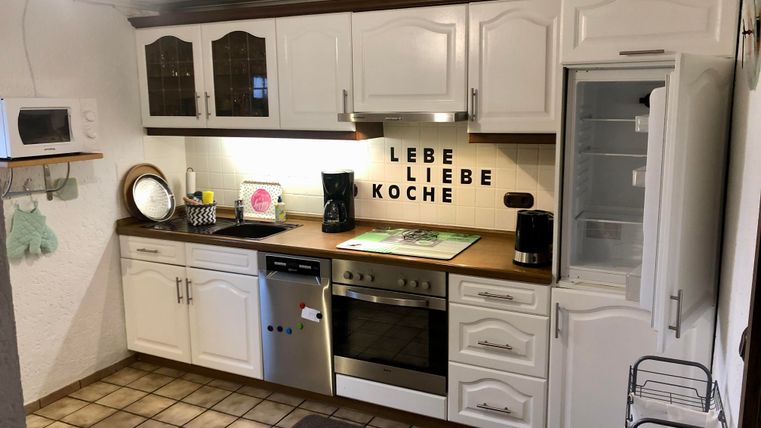 Une cuisine moderne avec des armoires blanches et un plan de travail en bois. Sur le mur se trouve la phrase "VIVRE AIMER CUISINER".