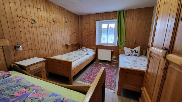 Ein einfaches Zimmer mit Holzverkleidung und zwei Einzelbetten. Es gibt ein Fenster mit einem grünen Vorhang und einen Teppich auf dem Boden.