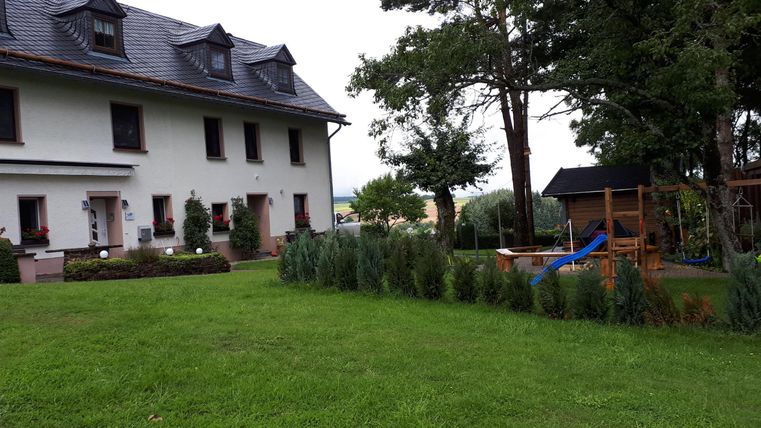 Ein schönes Haus mit einem großen Garten und viel Grün. Im Hintergrund befindet sich ein Spielplatz mit Rutsche.