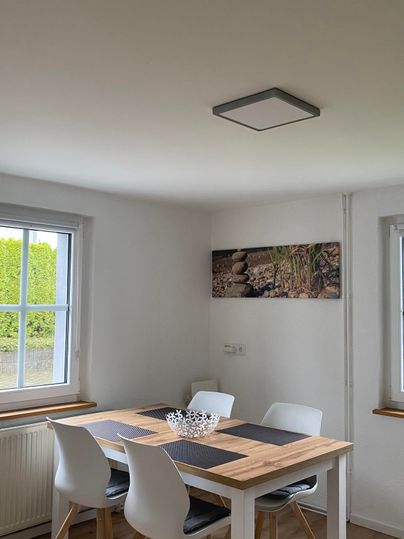 Ein helles Esszimmer mit einem Holztisch und weißen Stühlen. An der Wand hängt ein Gemälde.