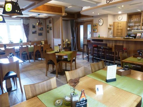 Ein gemütliches Restaurant mit Holzmöbeln und grünen Tischdecken. Die Wände sind mit Fotos dekoriert und eine Bar befindet sich im Hintergrund.