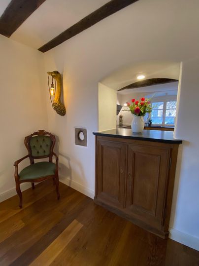 A cozy entrance area with a wooden floor. On a sideboard, there is a vase with colorful flowers, next to it a cushioned chair.