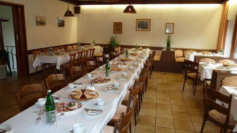 An inviting dining hall with long tables set with various dishes and drinks. The atmosphere is cozy with wooden chairs and warm lighting.