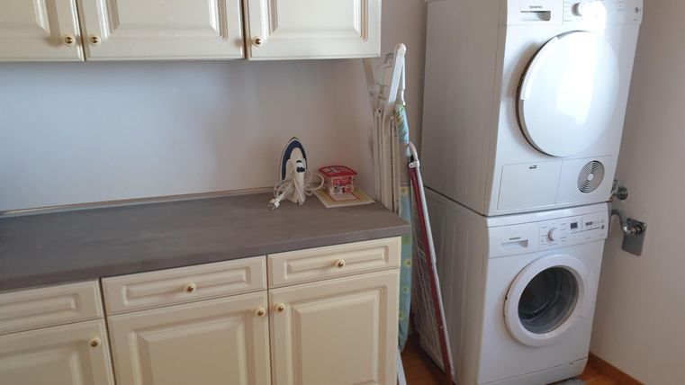 Ein funktionaler Waschraum mit einer Waschmaschine und einem Trockner. Auf der Arbeitsplatte stehen ein Bügeleisen und einige Utensilien.