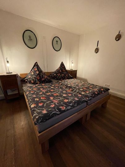 A cozy bedroom with a large bed and colorful pillows. The walls are decorated with round pictures, and there are nightstands with lamps.