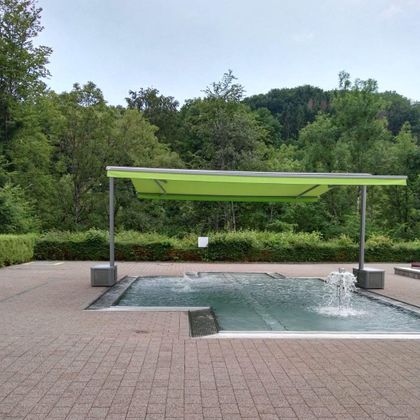 Ein moderner Wasserbereich mit einem grünen Sonnenschutz. Umgeben von Bäumen und Sträuchern in einer ruhigen Umgebung.