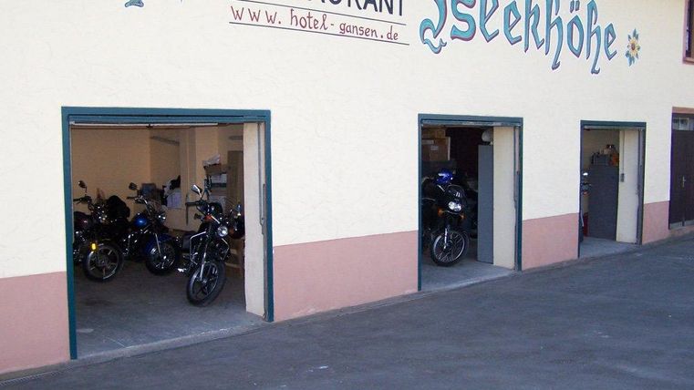 Een motorgarage met meerdere motoren staat op de voorgrond. Bovenaan bevindt zich het bord van een restaurant genaamd "Isekkhöhe".