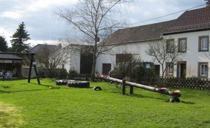 Ein gepflegter Garten mit einem Spielplatz und einem großen Rasen. Im Hintergrund sind mehrere Bäume und ein Wohnhaus zu sehen.