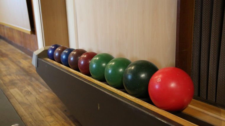 A series of colorful bowling balls is arranged on a wooden surface. The balls are laid out in various colors, including blue, green, red, and brown.
