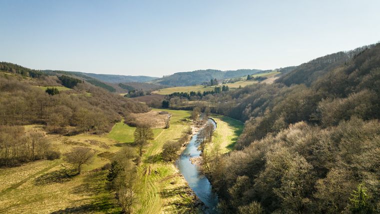 Landschaft mit Fluss, Wiesen und Hügeln unter blauem Himmel.