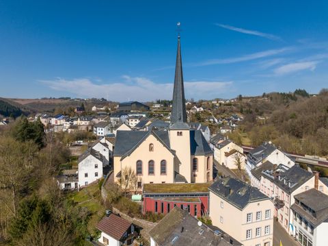 Eine kleine Stadt mit vielen Gebäuden und einer markanten Kirche im Vordergrund. Der Kirchturm ragt hoch in den klaren blauen Himmel.