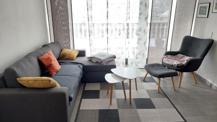 A modern living room with a gray sofa and a cozy armchair. Large windows let in plenty of light and the carpet creates a cozy atmosphere.