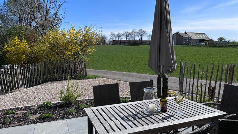 A beautiful garden with a table and chairs. In the background, green fields and a light blue sky can be seen.