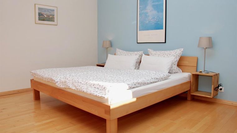 Une chambre confortable avec un lit en bois et une literie fraîche. La pièce a une atmosphère lumineuse et accueillante avec un mur bleu.