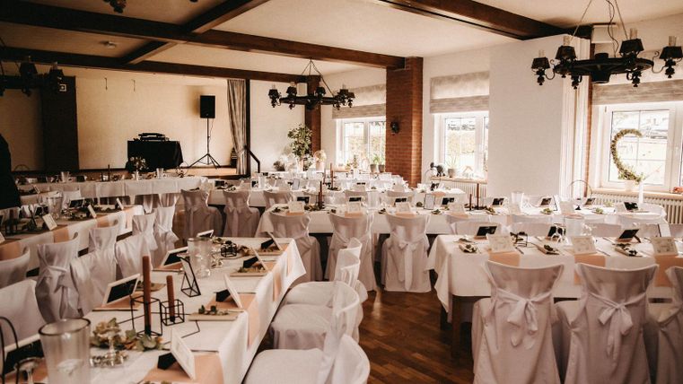 Ein eleganter Veranstaltungsraum mit festlich gedeckten Tischen und weißen Stühlen. Die Atmosphäre ist einladend und bereit für ein besonderes Event.