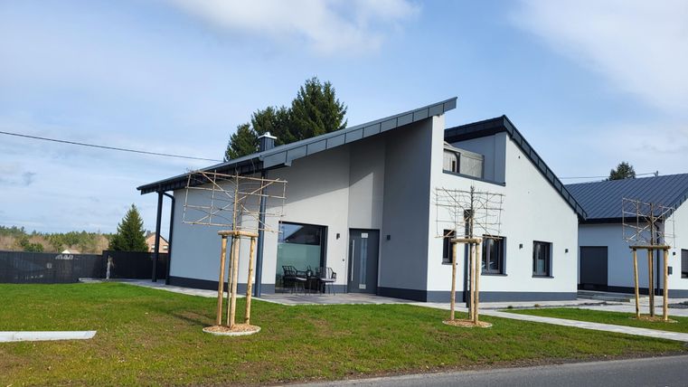 Ein modernes Einfamilienhaus mit einer hellen Fassade und einem pensionierten Dach. Der Garten ist gepflegt und es gibt eine Terrasse im Freien.