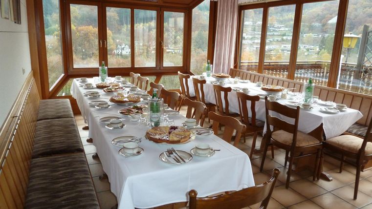 A bright restaurant with large windows. A long table is festively set and offers space for several guests.