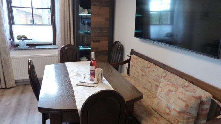 Ein gemütlicher Essbereich mit einem Holztablett, Stühlen und einem Sofa. An der Wand hängt ein großer Fernseher.