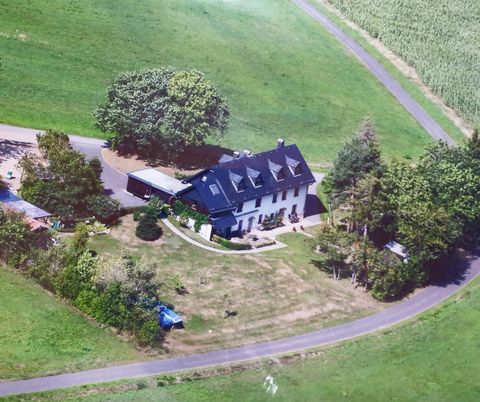 Ein großes, modernes Haus umgeben von grünen Wiesen und Bäumen. Die Auffahrt führt sanft zum Gebäude, das von einem gepflegten Grundstück umgeben ist.