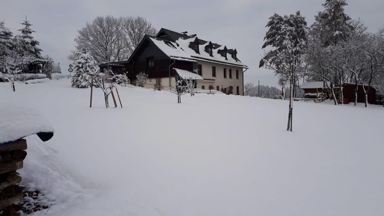 Ein schönes Haus in einer winterlichen Landschaft, umgeben von Schnee. Die Bäume sind mit einer weißen Decke überzogen, und der Himmel ist bewölkt.