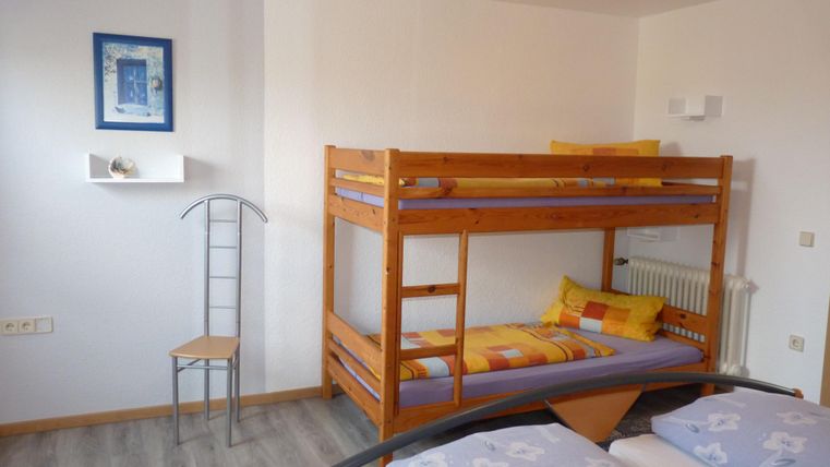 Une chambre simple avec un lit superposé et deux lits simples. Les murs sont clairs et il y a un cadre décoratif avec une image.