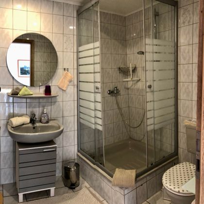 Une salle de bain moderne avec une douche et un lavabo. Les murs sont carrelés en blanc, et il y a un miroir rond ainsi qu'un toilette.