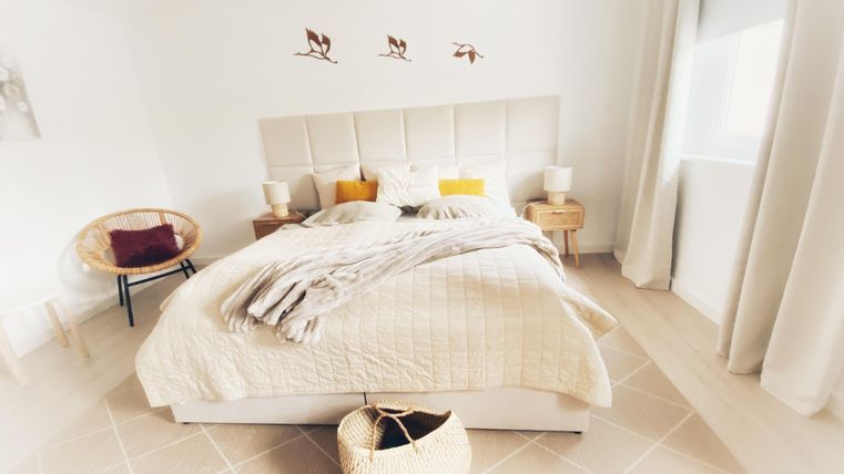 Een lichte slaapkamer met een comfortabel bed en gezellige decoratie. De muren zijn wit en er zijn enkele decoratieve elementen die een uitnodigende sfeer creëren.