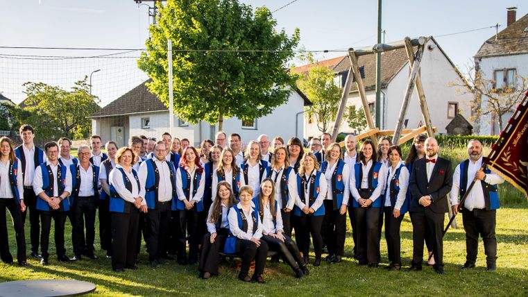 Eine große Gruppe von Menschen steht im Freien auf einer Wiese. Sie tragen blaue Westen und posieren lächelnd zusammen.