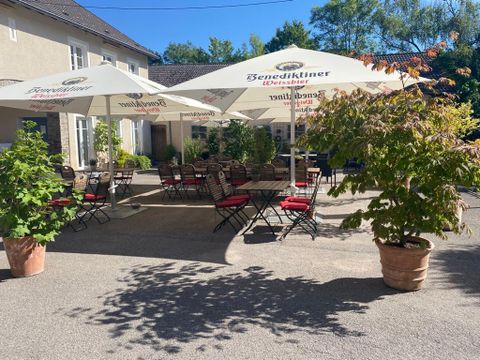 Ein gemütlicher Außenbereich mit Tischen und Stühlen unter großen Sonnenschirmen. Umgeben von Pflanzen bietet der Platz einen einladenden Eindruck für Gäste.