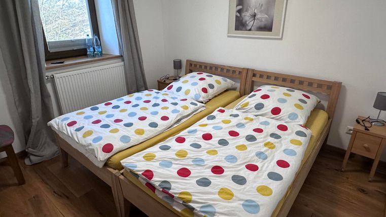 A cozy bedroom with two beds and colorful bed covers. The room has a window view and a simple, modern decor.