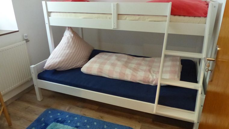 Ein Etagenbett mit weißen Rahmen und bunten Bettwäsche. Der Raum hat einen hellen und einladenden Look.