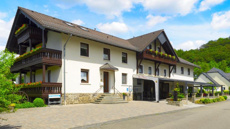 Ein modernes Gebäude mit mehreren Etagen und Balkonen, umgeben von grüner Natur. Der Himmel ist blau mit einigen Wolken.