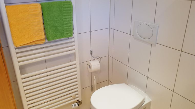 Ein sauberes Badezimmer mit einer Toilette und Handtüchern in verschiedenen Farben. An der Wand ist ein Handtuchheizkörper sichtbar.