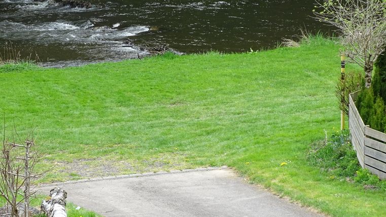 Ein ruhiger Fluss fließt durch eine grüne Wiese. Am Ufer befinden sich einige Bäume und ein schmaler Weg.