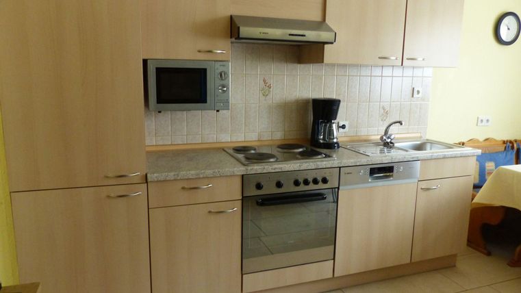 Eine moderne Küche mit Holzschränken und Edelstahlgeräten. Sie enthält einen Herd, einen Ofen, eine Mikrowelle und eine Kaffeemaschine.