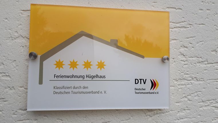 Ein Schild mit der Aufschrift „Ferienwohnung Hochhaus“ und drei goldenen Sternen. Das Schild ist von der Deutschen Tourismuszentrale e.V. genehmigt.